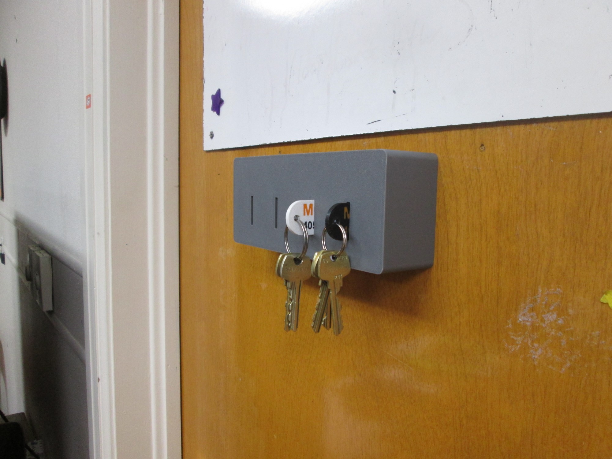 3D-printed key box mounted on the office door with two labeled key sets hanging from it