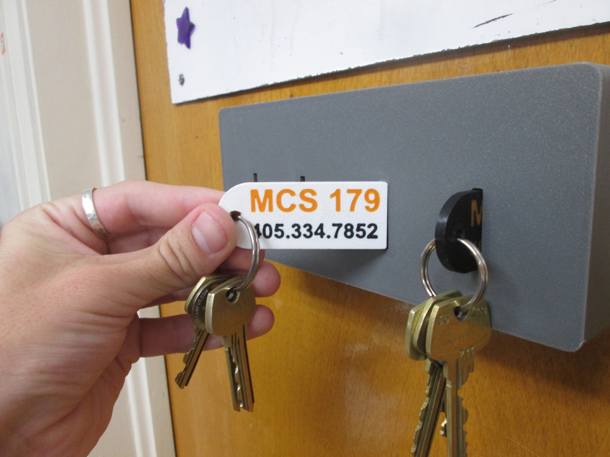 Close-up of a keychain tag printed with the room number and phone number, held next to the mounted box